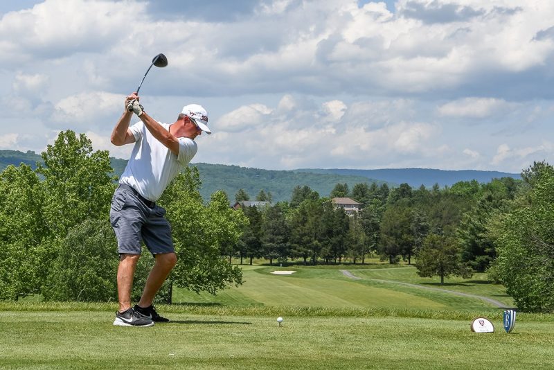 Golfer taking a swing at the 2019 Hokie Cow Classic. Blue skies, fluffy clouds, green trees and lush course.
